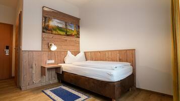 Une chambre avec une tête de lit en bois, un tableau au-dessus du lit, une lampe de chevet et un tapis bleu sur le sol.