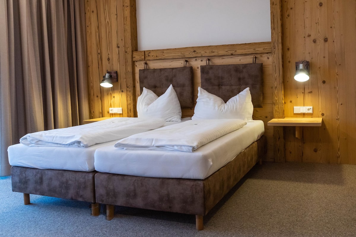 A double bed with two pillows, a wooden headboard, and two bedside lamps.