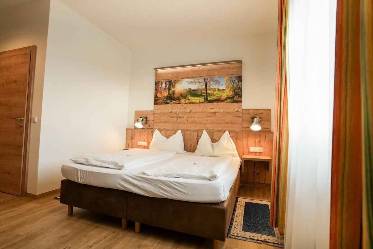A bedroom with a wooden headboard, a bed with white linens, two bedside lamps, and a painting above the bed.
