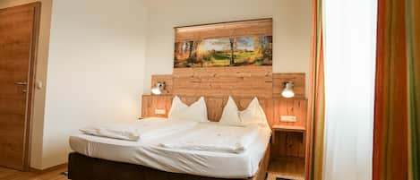Un dormitorio con cabecera de madera, cama con ropa de cama blanca, dos lámparas de noche y un cuadro sobre la cama.
