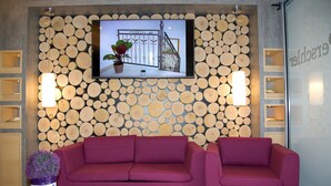 A modern interior with a wooden log wall, a television, a purple sofa, and a small table with a magazine. - Hotel Restaurant Perschler (Fohnsdorf)