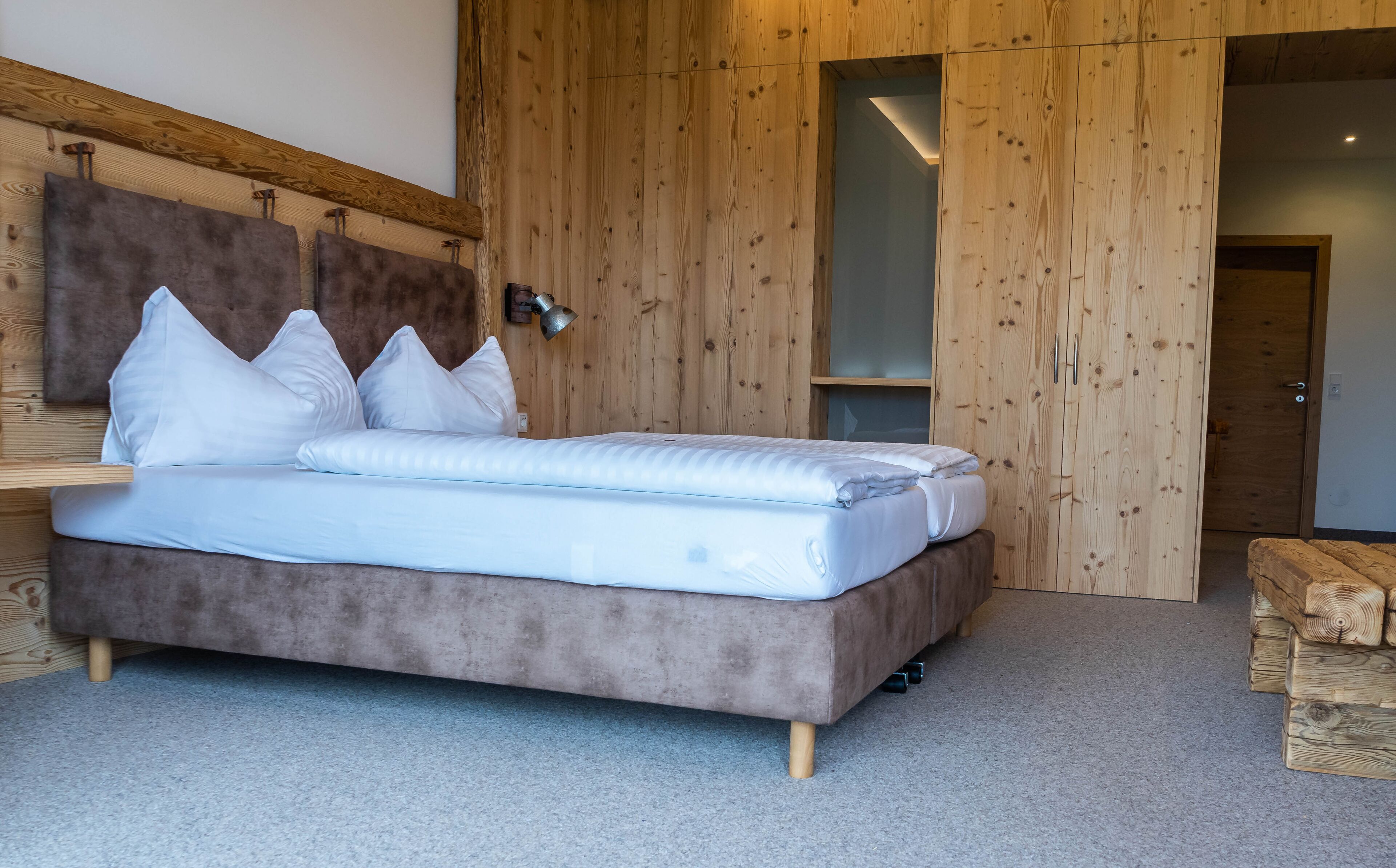 Una cama con ropa de cama blanca, un cabecero de madera y una alfombra gris.
