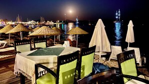 Un restaurante frente al mar con terraza, mesas, sillas y sombrillas.