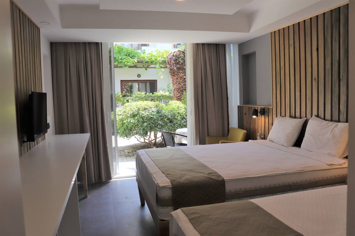 Ein Hotelzimmer mit einem großen Bett, einem Schreibtisch und einem Fernseher. Blick auf einen Garten und ein Gebäude vor dem Fenster.
