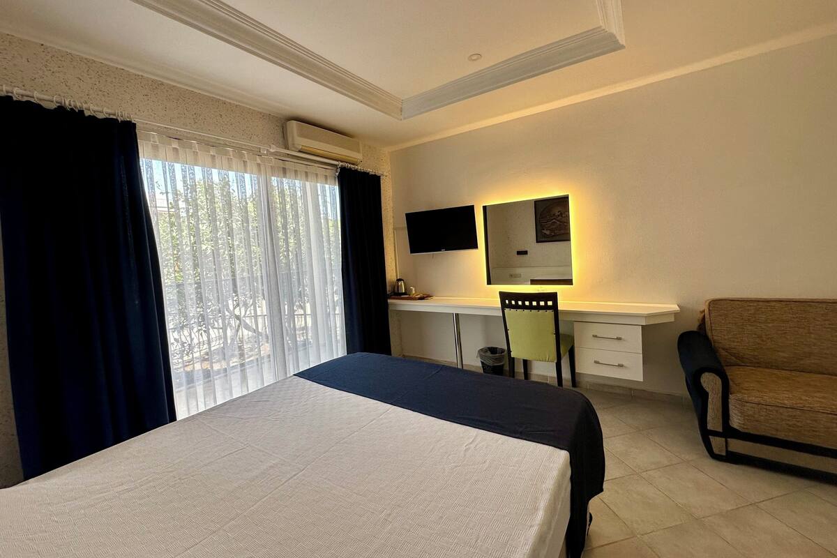 Ein Hotelzimmer mit einem Bett, einem Schreibtisch mit Stuhl, einer Couch, einem Fernseher und einer Klimaanlage.