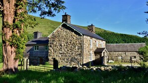 A stone building with a sloped roof, a wooden fence, and a large tree in the foreground. - The Firecat Country House B&B (Machynlleth)
