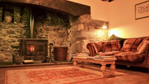 A cozy living room with a stone wall, a fireplace, a plaid sofa, and a wooden coffee table. - The Firecat Country House B&B (Machynlleth)