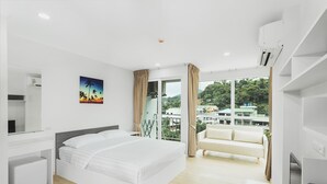 Habitación de hotel moderna con una cama grande, un escritorio, una silla y un balcón con vistas a la ciudad.