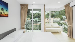Un dormitorio con una cama grande, un sofá y un balcón con vistas a edificios y vegetación.