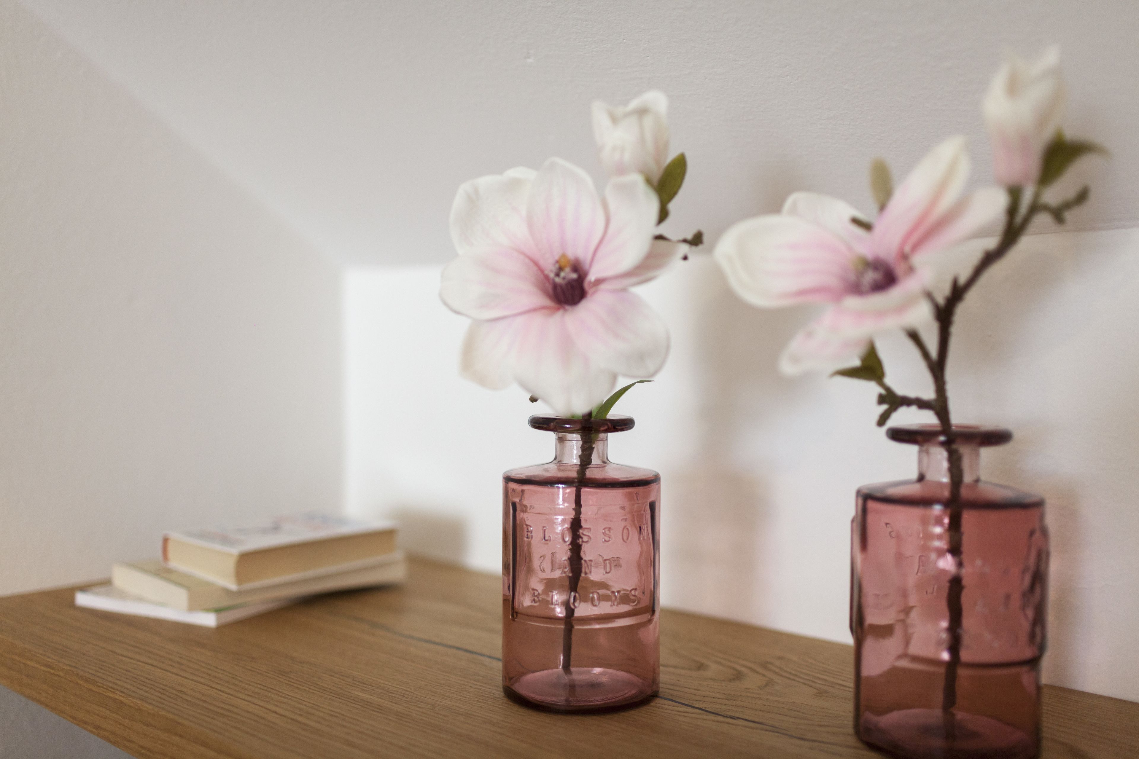 Dos jarrones de vidrio rosa con flores sobre una superficie de madera.