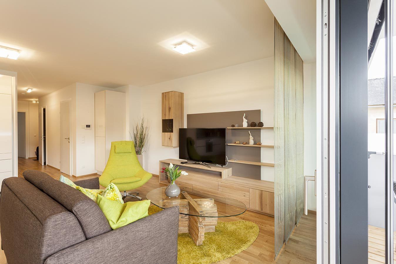 Ein modernes Wohnzimmer mit einer Couch, einem grünen Sessel, einem Fernseher und einem Holzschrank.
