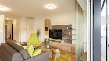 Ein modernes Wohnzimmer mit einer Couch, einem grünen Sessel, einem Fernseher und einem Holzschrank.