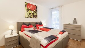 Un dormitorio con cama, mesitas de noche, cómoda, ventana con cortinas y una estatua de Buda.