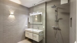 Un baño moderno con ducha envuelta en vidrio, tocador doble y un espejo grande.