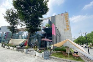Un bâtiment moderne doté d’une façade en verre, d’un espace extérieur aménagé pour s’asseoir et d’une enseigne avec des caractères chinois.