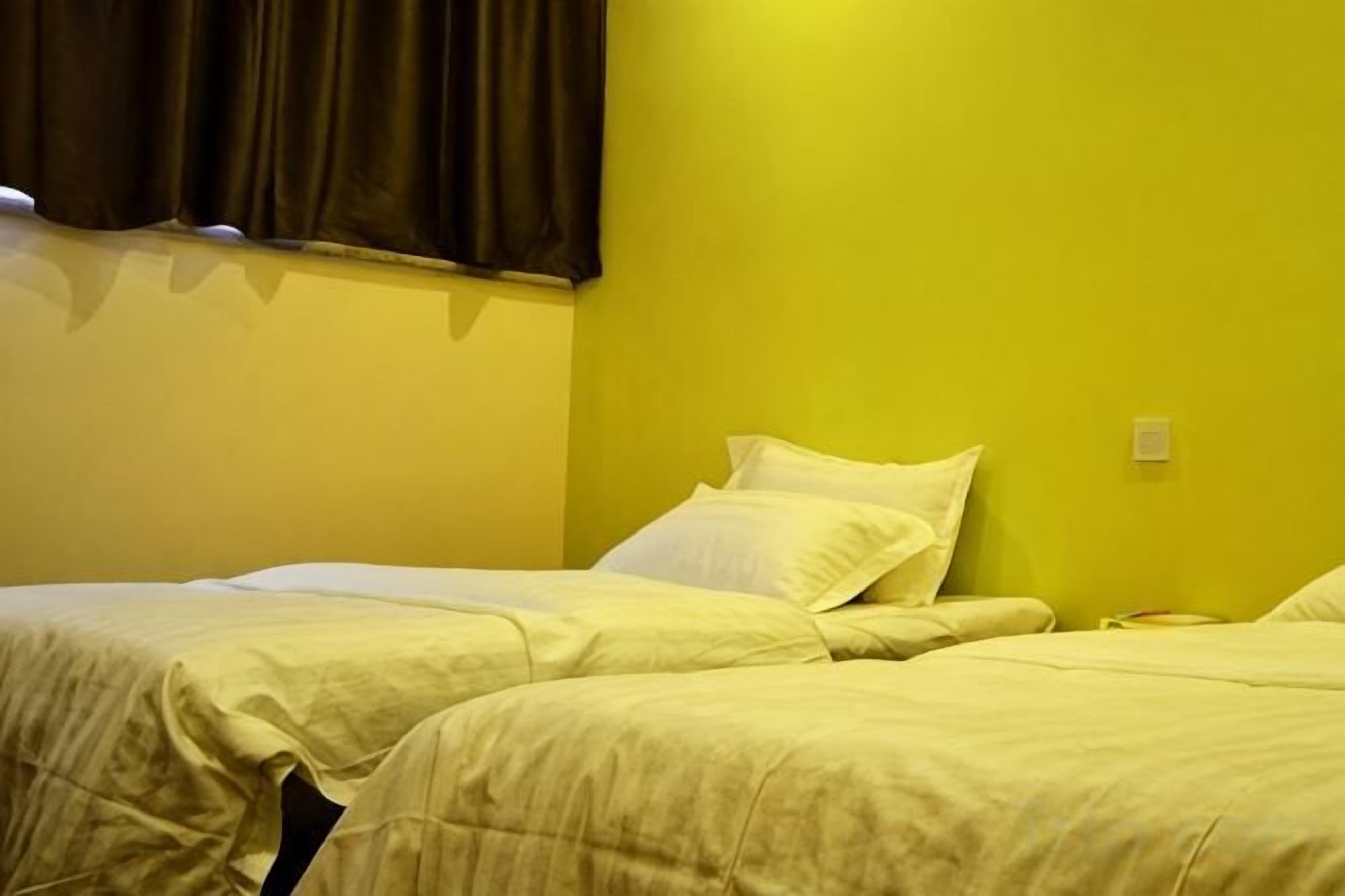 Une chambre avec deux lits, une fenêtre avec des rideaux et un interrupteur sur le mur.