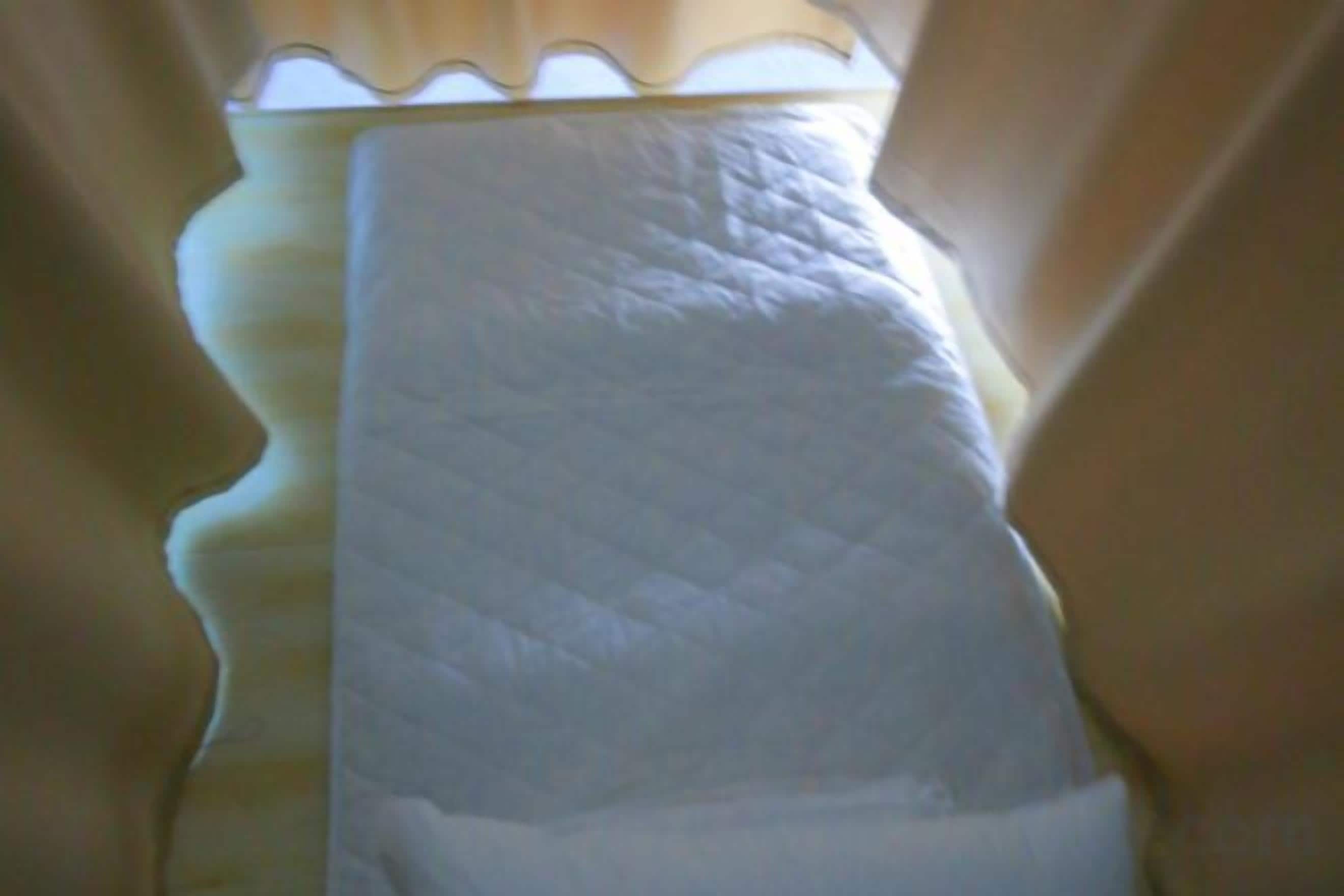 Un coussin blanc orné d’un motif matelassé, dont on aperçoit une partie à travers une fenêtre à motifs ondulés.