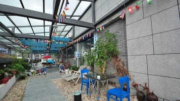 Un espace extérieur abrité, aménagé avec des sièges, des plantes en pot et une structure de plafond en verre.
