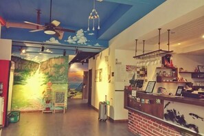 Un vestíbulo de hotel con un mural, una recepción y un ventilador de techo.
