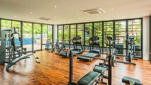 Une salle de sport spacieuse, dotée de divers appareils d’exercice, de grandes fenêtres et d’un plancher en bois.