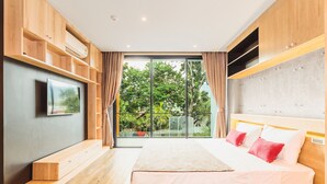 Une chambre moderne dotée d’un grand lit, d’étagères intégrées, d’un téléviseur à écran plat et d’une porte-fenêtre coulissante donnant sur un balcon avec vue sur les arbres.