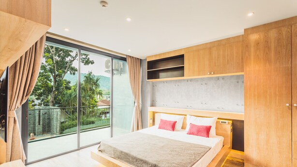 Une chambre moderne avec un grand lit, une tête de lit en bois et une porte-fenêtre coulissante donnant sur un balcon.