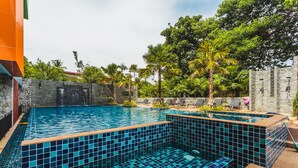 Une piscine dont le fond est recouvert de carreaux bleus et turquoise, entourée de chaises longues et de palmiers.