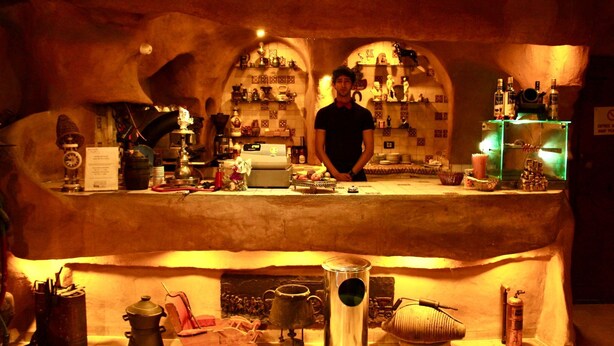 A bar area with a bartender, shelves with bottles, and various bar equipment. - Hotel Donia (Hammam Chatt)