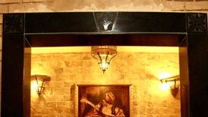 A lobby with a stone wall, a painting of a woman and child, and two wall-mounted lamps. - Hotel Donia (Hammam Chatt)