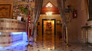 A lobby with a tiled floor, a reception desk, a chandelier, and a wall with photographs and keys. - Hotel Donia (Hammam Chatt)