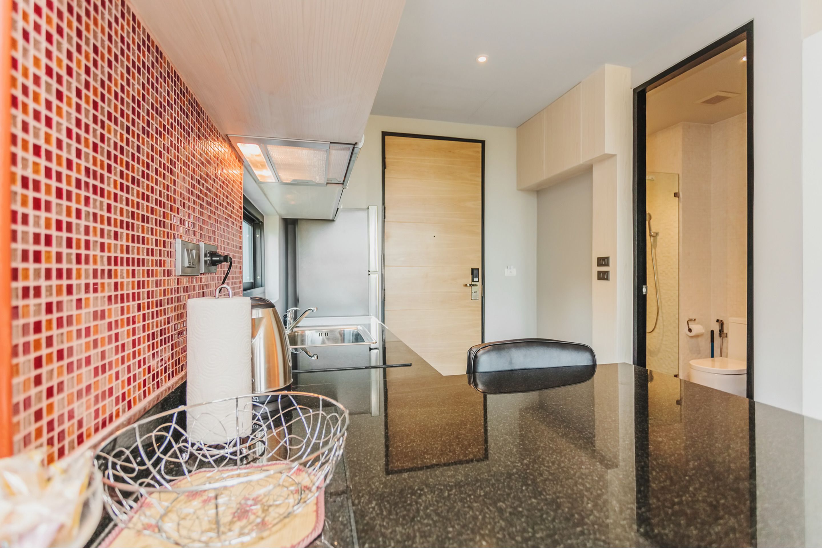 Een moderne hotel lobby met een betegelde muur, een receptiebalie, een zithoek en een zichtbare badkamer.