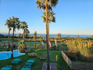 A pool area with chairs and tables, palm trees, and a view of the ocean. - WaWa Tarifa (Tarifa)