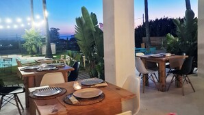An outdoor dining area with tables and chairs, a pool, and palm trees. - WaWa Tarifa (Tarifa)