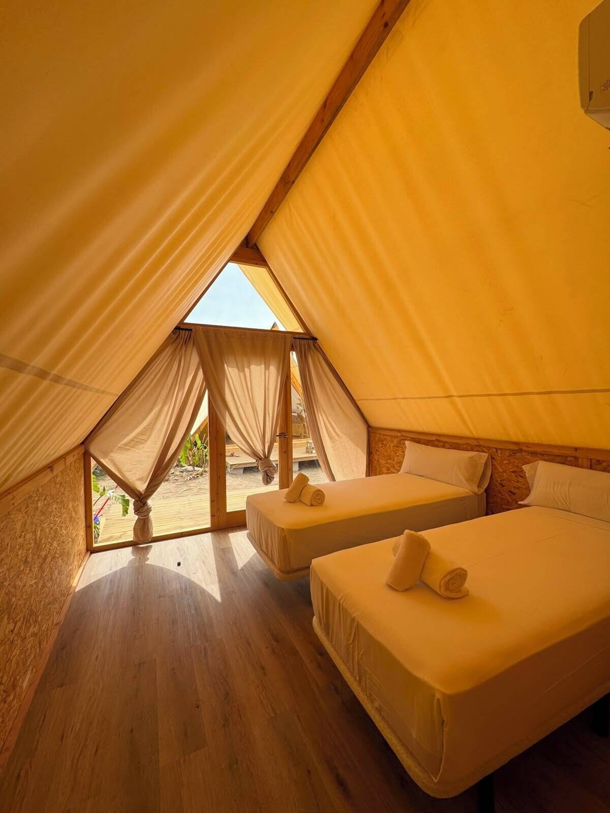 Een tentaccomodatie met twee bedden, houten vloeren en uitzicht op de natuur.