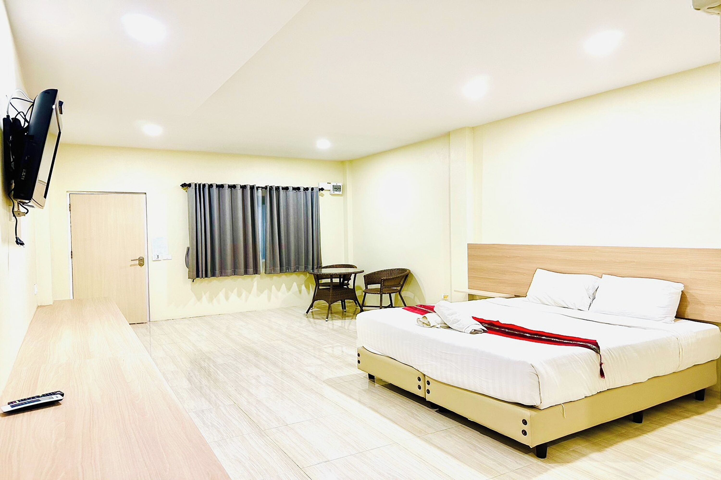 Quarto de hotel com cama, escrivaninha, cadeira, televisão e janela com cortinas.