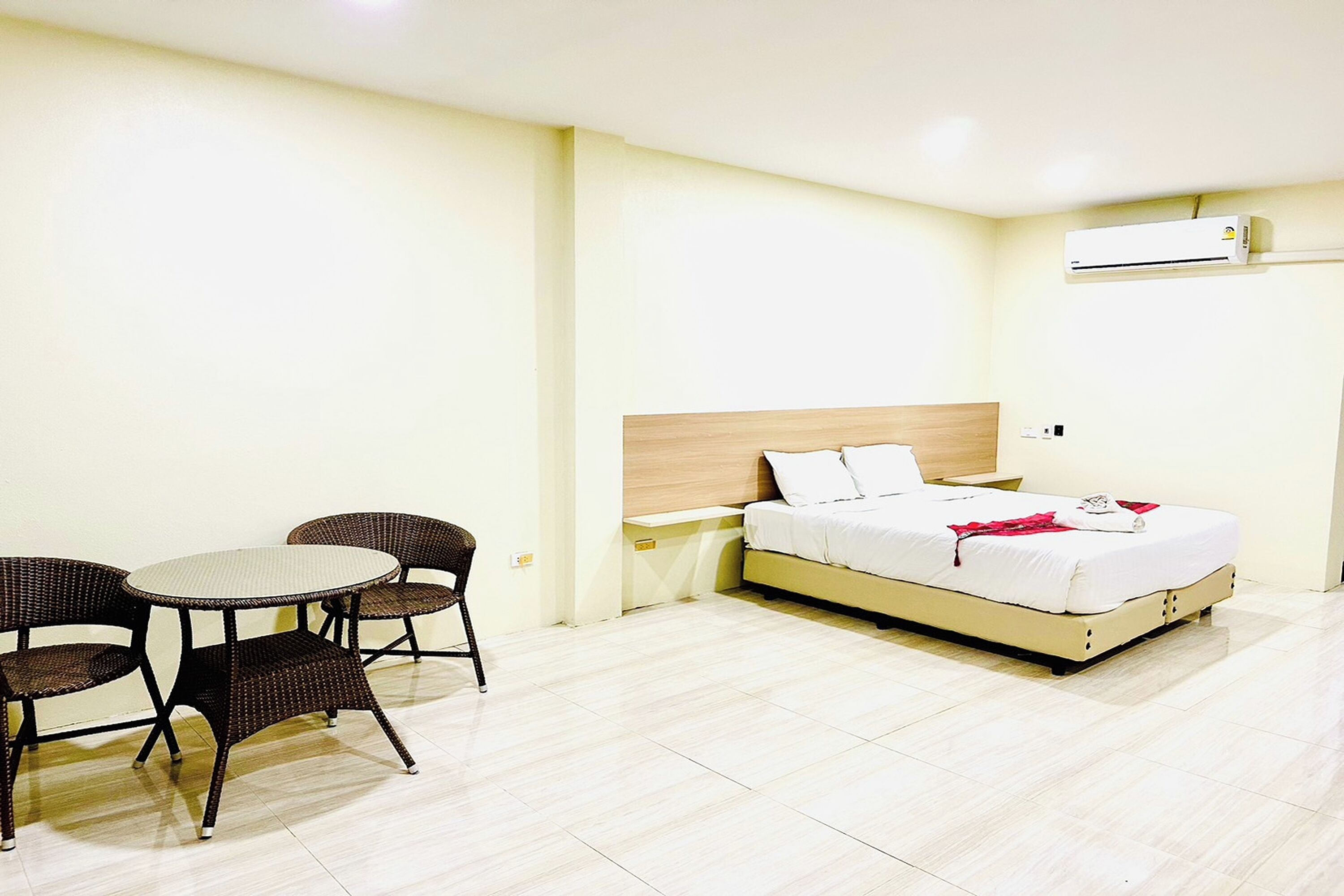A hotel room with a bed, a round table with chairs, and an air conditioning unit.