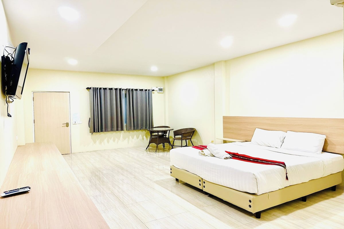 Ein Hotelzimmer mit einem Bett, einem Schreibtisch, einem Stuhl, einem Fernseher und einem fensterbepflanzten Fenster.