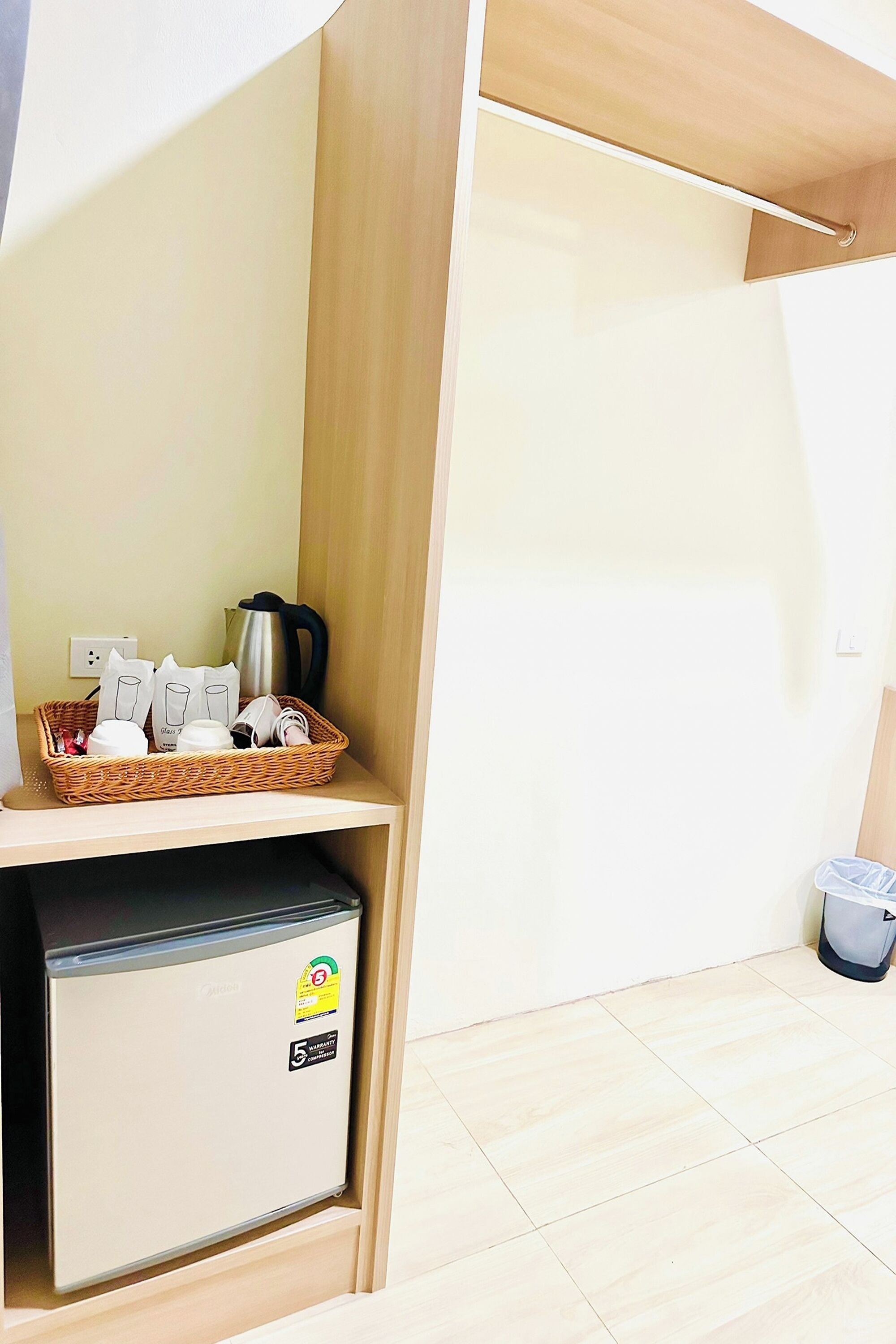 A kitchenette with a refrigerator, a coffee maker, and a basket of items on a shelf.