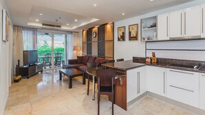 A modern hotel room with a dining area, a sofa, a TV, and a balcony with a view of greenery. - Condo in Panwa in Bel Air - Unit C204 (Wichit)