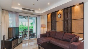 A modern living room with a sofa, TV, and a dining area with chairs and a table. - Condo in Panwa in Bel Air - Unit C204 (Wichit)