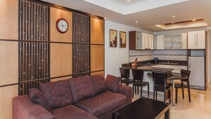 A modern living room with a sofa, a coffee table, and a dining area with chairs and a small kitchen in the background. - Condo in Panwa in Bel Air - Unit C204 (Wichit)