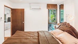 A bedroom with a wooden wardrobe, a bed with a brown headboard, a window with a view of greenery, and an air conditioning unit on the wall. - Condo in Panwa in Pixels 89-230 (Wichit)
