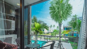 A balcony with a view of a swimming pool, palm trees, and modern buildings. - Condo in Panwa in Pixels 89-230 (Wichit)