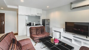 A modern living room with a sofa, a coffee table, a flat-screen TV, and a kitchen area with cabinets and appliances. - Condo in Panwa in Pixels 89-230 (Wichit)