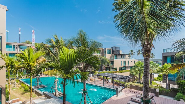 A modern hotel with a rooftop pool surrounded by palm trees and lounge chairs. - Condo in Panwa in Pixels 89-230 (Wichit)