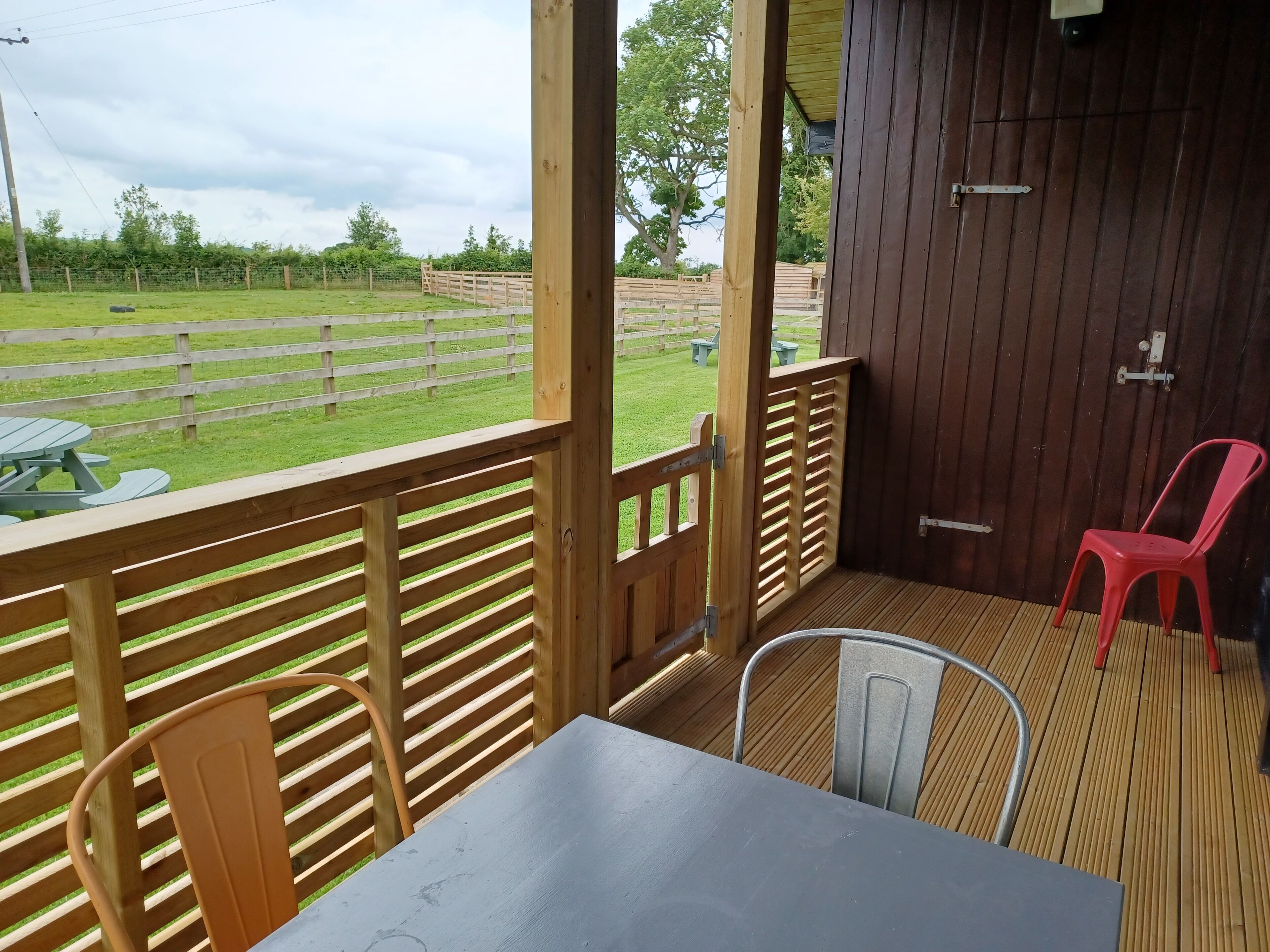 Un espace extérieur abrité, doté d’une table et de chaises, d’une clôture en bois et offrant une vue sur un champ verdoyant.