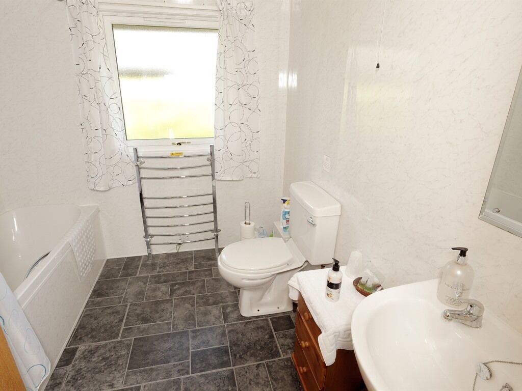 Un baño con bañera, inodoro, lavamanos y ventana con cortinas.