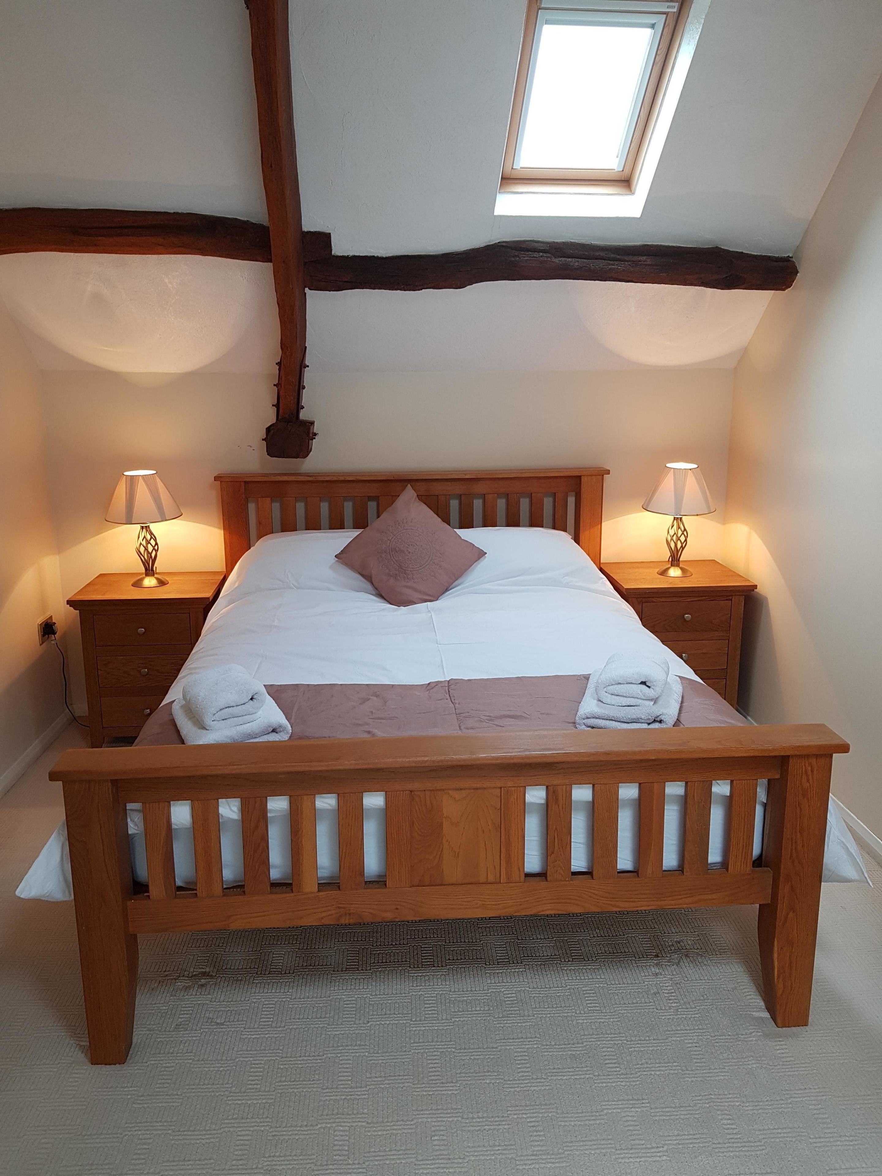 A bedroom with a wooden bed, two bedside tables with lamps, a skylight, and a view of the sky.