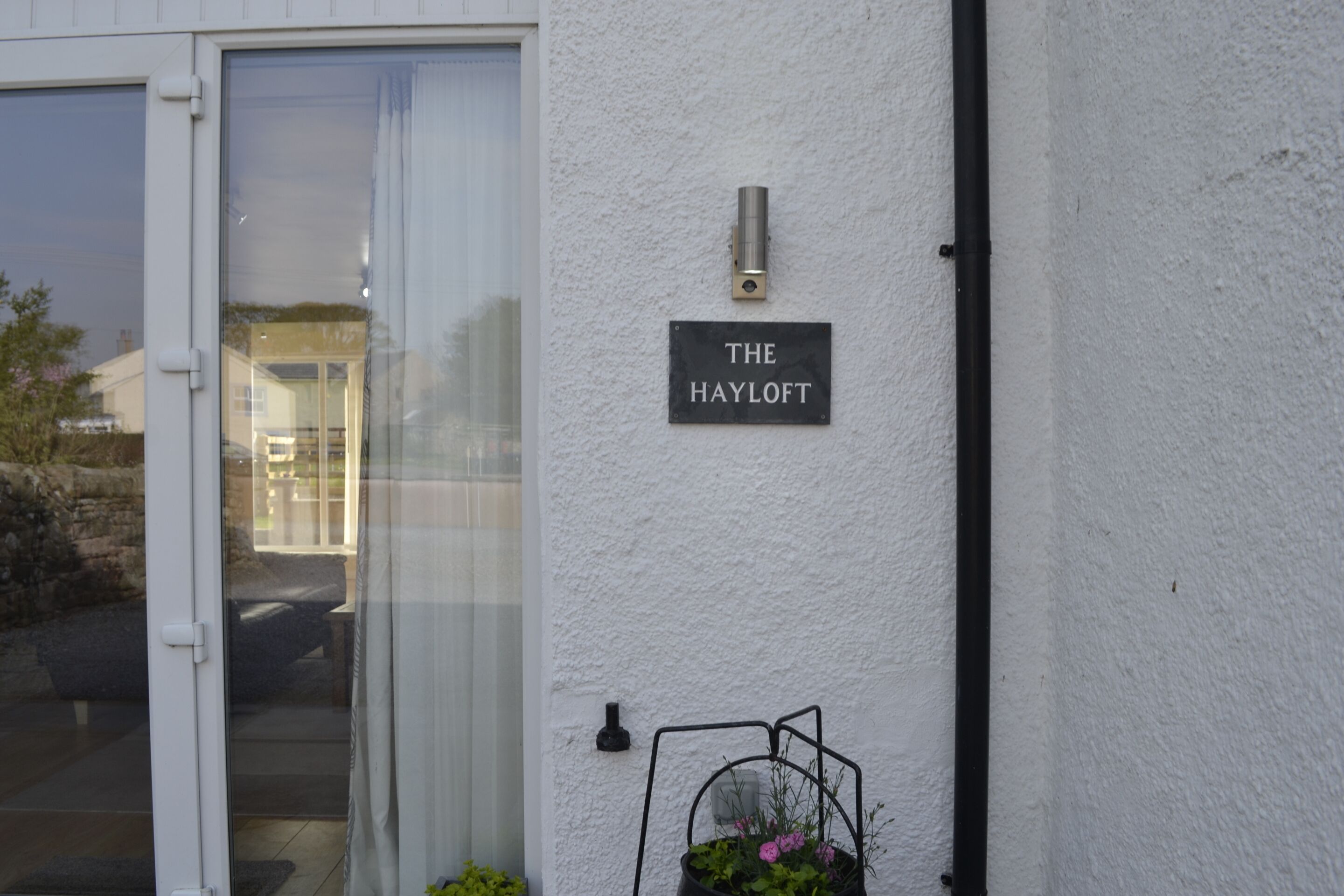 Pared exterior blanca con una puerta, un letrero que dice "THE HAYLOFT" y un accesorio de luz exterior negro.