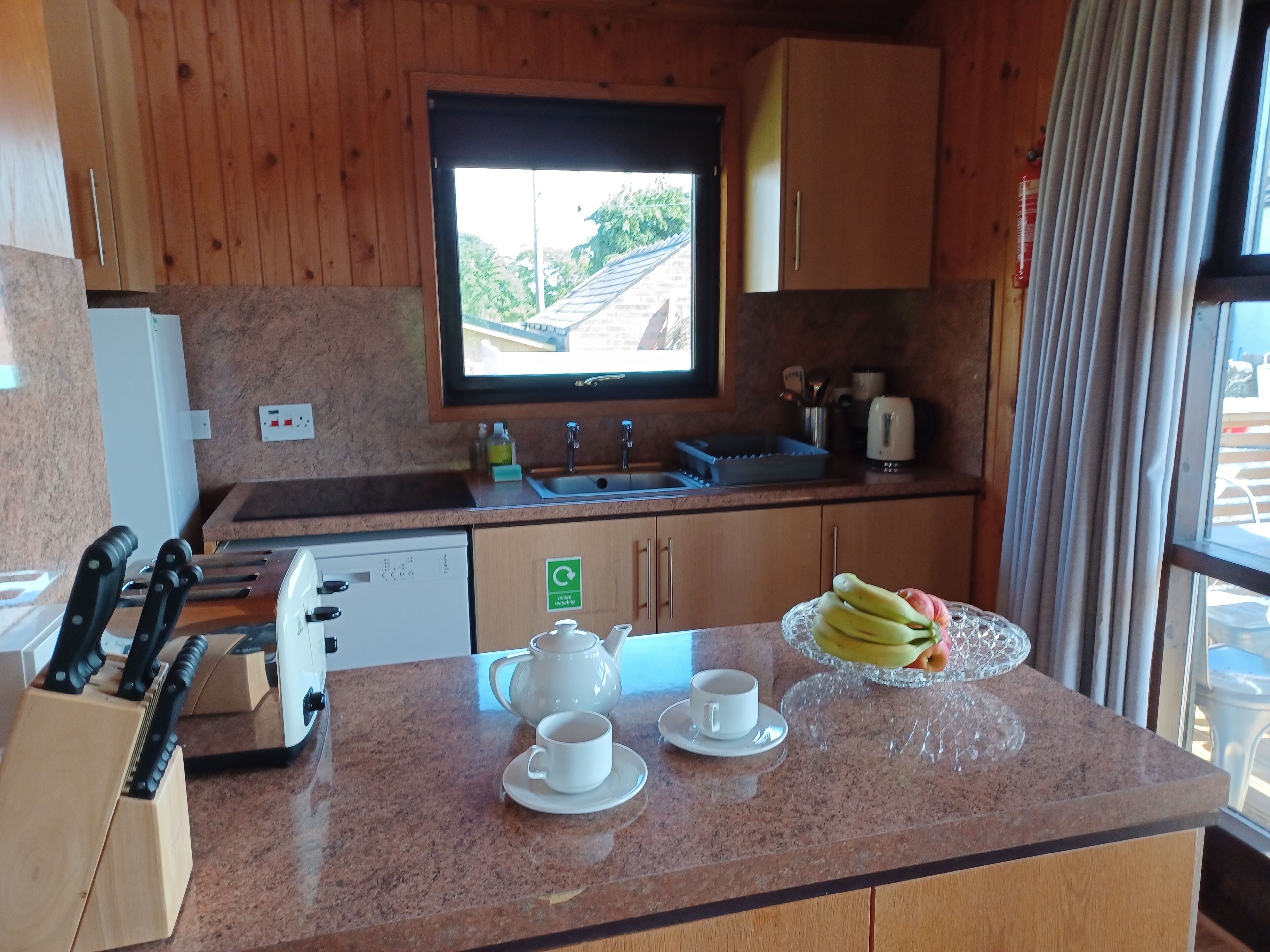 A kitchen with wooden cabinets, a window, a sink, a toaster, a coffee maker, and a fruit bowl on the counter.